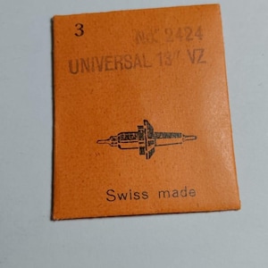 May include: A white ceramic mug with a black handle and the text "But First, Coffee" in a bold, black font. The mug is set against a blurred background. The mug appears to be approximately 10 cm tall.