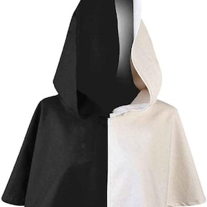 Könnte beinhalten: Ein Kapuzencape mit geteiltem Design, bei dem eine Hälfte in einfarbigem Schwarz und die andere Hälfte in Off-White gehalten ist. Das Kleidungsstück hat eine spitze Kapuze und eine kurze, ausgestellte Silhouette bis zum Oberkörper.