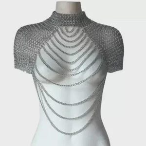 Puede incluir: Top de cota de malla plateada con cuello alto y mangas cortas. El área del pecho presenta múltiples hilos de cadenas drapeadas, creando un efecto en capas. La prenda se exhibe en un maniquí.