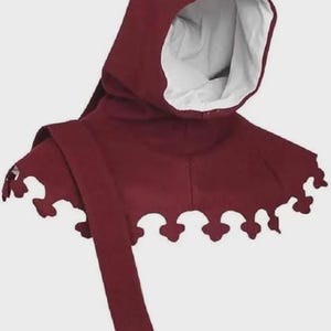 May include: Burgundy-colored medieval hood with a white interior lining. The hood features a decorative, scalloped edge along the shoulders and a long, flowing tie. This historical garment is suitable for cosplay or themed events.