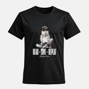 Könnte beinhalten: Schwarzes T-Shirt mit einer Aquarellillustration einer lesenden Person. Der Text "READ • LOVE • REPEAT" und "Literary Lover" sind darunter in Weiß gedruckt. Ein literarisches Design.
