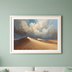 May include: A framed print of a desert landscape with sand dunes and a cloudy sky. The artwork hangs above a white sofa with green and cream cushions. A white lamp and side table are positioned to the left.