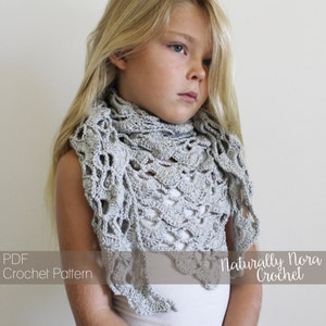 May include: A gray crochet shawl with a delicate lace pattern. The shawl is worn by a young girl with long blonde hair. The text "Naturally Nora Crochet" is visible in the bottom right corner of the image.
