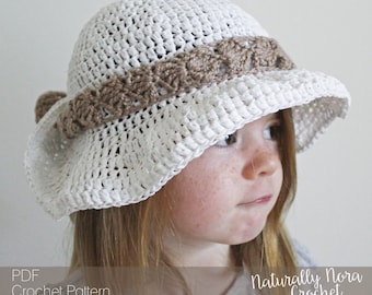 May include: White crochet sun hat with a brown crochet trim. The hat is worn by a child with brown hair. The text "Naturally Nora Crochet" is visible in the bottom right corner of the image.
