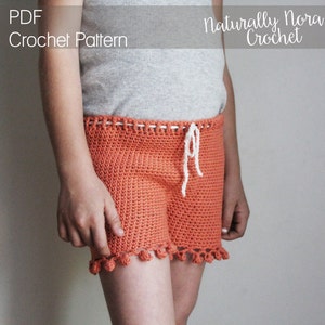 May include: A crochet pattern for a pair of orange shorts with white pom-poms on the bottom hem. The shorts have a white drawstring and are made with a simple stitch.