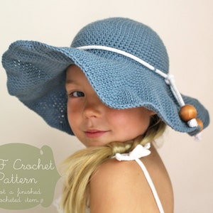 May include: A blue crochet sun hat with a white rope trim and wooden beads. The hat is worn by a child with blonde hair.