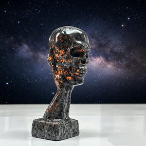 K&ouml;nnte beinhalten: Eine dunkelgraue Totenkopfskulptur mit orangefarbenen Akzenten, vor einem Sternenhintergrund. Der Sch&auml;del weist detaillierte Z&auml;hne und Augenh&ouml;hlen auf und ist auf einem rechteckigen Sockel montiert. Die Skulptur hat eine raue, steinartige Textur.