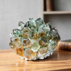 以下が含まれることがあります： 半透明の緑色と琥珀色のグラデーションが特徴的な、原石のクォーツクリスタルクラスター。この鉱物標本は、中心の基部から外側に向かって放射状に伸びる、多数の尖った多面的な結晶ポイントで構成されており、全体として球状の形状を形成しています。