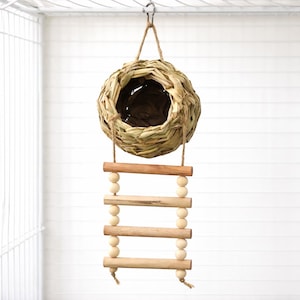 May include: A hanging bird nest crafted from woven natural materials, with a small wooden ladder. The nest is spherical with an opening, and the ladder features wooden rungs and small wooden beads. It hangs from a metal hook.