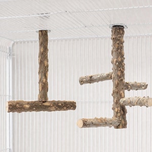 Könnte beinhalten: Zwei Vogelstangen aus Holz mit natürlicher Rindenstruktur, die an einem weißen Drahtkäfig aufgehängt sind. Eine Stange ist T-förmig, die andere hat mehrere Äste, die von einem zentralen Pfosten ausgehen.