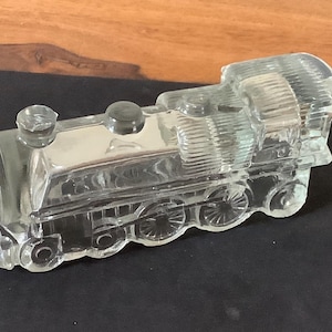 May include: A clear glass train engine figurine with detailed wheels and a textured surface.