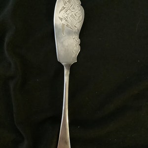 May include: A silver butter knife with an ornate floral design etched into the blade. The handle is plain and has the number "188" engraved on the bottom.