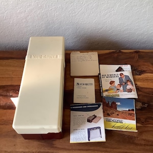 May include: A vintage View-Master viewer with a white and red case, along with several instruction manuals and a reel list. The manuals include "View-Master United Stereo Viewer Operating Instructions" and "See a World of Wonders".