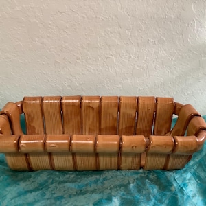 May include: A rectangular ceramic basket with a glossy light brown finish. The design features vertical slats that resemble bamboo or wood grain, with rounded edges forming the rim and base, creating a structured, open-top container.