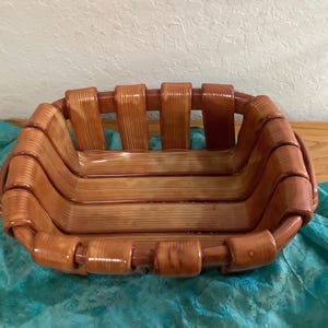 May include: A rectangular basket constructed from smooth, light brown wooden slats with a visible grain pattern. The design features vertical slats forming the sides and horizontal slats forming the base, connected by rounded, cylindrical wooden joints.