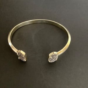 May include: A gold-toned bangle bracelet with a pave-set design on the ends. The bracelet is engraved with the words "Kendra Scott".