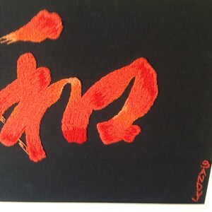 Puede incluir: Caligrafía china bordada en rojo sobre fondo negro. La caligrafía está enmarcada en un marco blanco. La firma "LCZCY" está en la esquina inferior derecha.