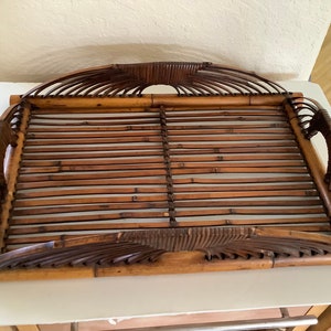 May include: A large, rectangular bamboo serving tray with intricate woven details and curved handles. The tray is made of natural brown bamboo.