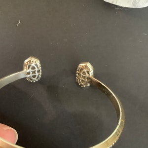 May include: Gold bangle bracelet with a decorative design on each end. The bracelet has a beaded edge.