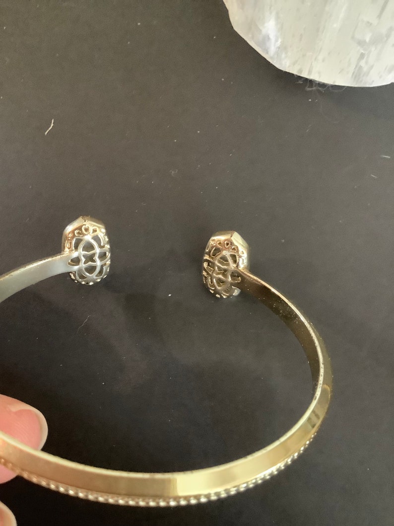 May include: Gold bangle bracelet with a decorative design on each end. The bracelet has a beaded edge.