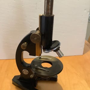 May include: A black vintage microscope with a brass stage and a black and brass body. The microscope has a single lens and a black base.