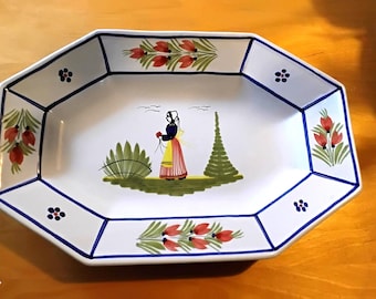 May include: White ceramic serving dish with an octagonal shape and a hand-painted design. The rim is outlined in blue, with floral and geometric patterns. The center features a figure in traditional attire.