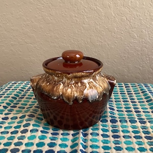 May include: A brown and white glazed ceramic cookie jar with a lid. The jar has a rustic, hand-painted look with brown and white swirls.