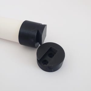 May include: A white cylindrical object with a black cap and a separate black circular base. The base has two small holes and a square indentation. The objects are on a white surface.