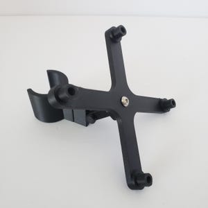 May include: A black, 3D-printed device with a cross-shaped design and a curved support. The device has four cylindrical extensions at the ends of the cross arms and a central screw. The curved support is on the left side.
