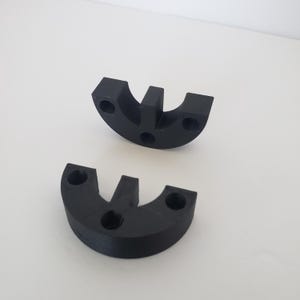May include: Two black, semi-circular objects with a central vertical protrusion and three circular holes. The objects are made of a solid material and are positioned on a white surface.