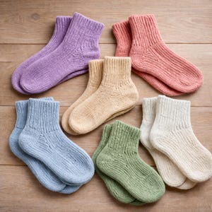 May include: Seven pairs of knitted socks in a variety of colours, including lavender, peach, tan, light blue, green, and off-white. The socks are displayed on a wooden surface, highlighting their textured knit design and cosy appearance.