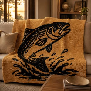 May include: Mustard yellow knitted throw blanket featuring a large black graphic of a leaping fish. The blanket is draped over a beige sofa, with a wooden coffee table in the foreground. The blanket's design is suitable for a cabin or lodge.