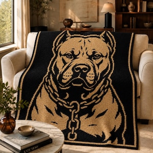 May include: A black and tan throw blanket featuring a detailed graphic of a dog's face. The dog is depicted with a chain collar. The blanket is draped over a beige sofa. The throw has a border of tan stripes.