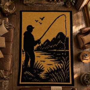 May include: A knitted throw blanket featuring a black silhouette of a person fishing on a golden yellow background. The design includes a fishing rod, lake, mountains, and birds. The blanket has a black border.