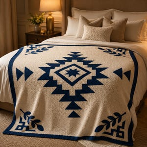 May include: A cream-colored knitted blanket with a geometric design in navy blue. The blanket features a central diamond shape with a star, surrounded by triangles and other shapes. The border and edges are also navy blue.