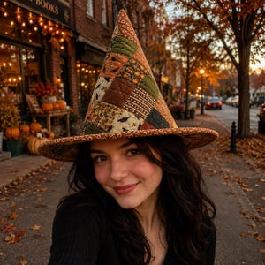 May include: A tall, pointed witch hat featuring a quilted patchwork design with various autumn-themed fabric patterns in shades of orange, brown, green, and cream. The hat has a wide, flat brim and a structured, conical crown with visible stitching.