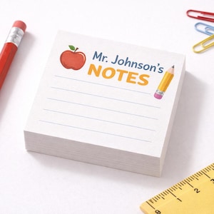 Könnte beinhalten: Ein Stapel weißes Notizpapier mit dem Text "Mr. Johnson's NOTES" und einem Apfel-Grafik. Ein roter Bleistift, ein gelbes Lineal und bunte Büroklammern sind ebenfalls vorhanden. Ideal für Schule oder Büro.