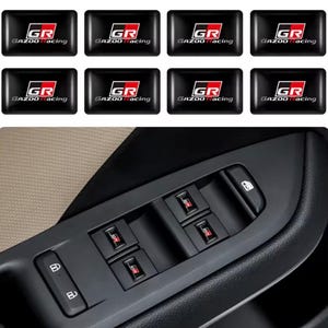 Könnte beinhalten: Schwarze rechteckige Aufkleber mit dem Text "GR GAZOO Racing" in Weiß und Rot. Die Aufkleber werden in einer Gruppe und auch auf der Fensterbedienkonsole eines Autos gezeigt.