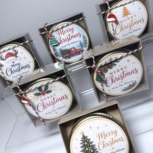 May include: Five round metal tins in clear boxes, each with a custom label reading Merry Christmas From The Wilsons. Designs include a red truck, a reindeer, holly, a pine tree, and a Santa hat. Each tin is tied with red, green, and white twine.