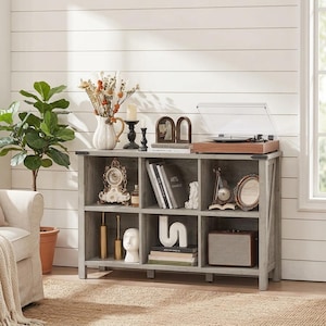 May include: A gray wooden six-compartment storage unit with a record player on top. The shelves contain a clock, books, a white abstract sculpture, a small mirror, and a speaker. The unit features X-shaped side supports and metal corner accents.