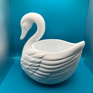 May include: A matte white swan-shaped planter or decorative bowl featuring a long, curved neck and detailed molded feather textures on the wings. The interior is smooth and hollow, providing an open basin for holding small items or plants.