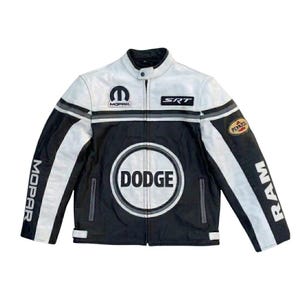 May include: Black and white leather jacket with a stand-up collar. The jacket features the Dodge logo on the chest, Mopar and SRT patches, and Penzoil and RAM branding. The jacket has a zip-up front and a classic racing design.