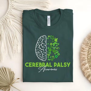 Op de afbeelding: Donkergroen t-shirt met een witte hersengrafiek aan de linkerkant en een groen bloemen- en vlinderontwerp aan de rechterkant. De woorden "CEREBRAL PALSY Awareness" zijn groen en wit gedrukt.