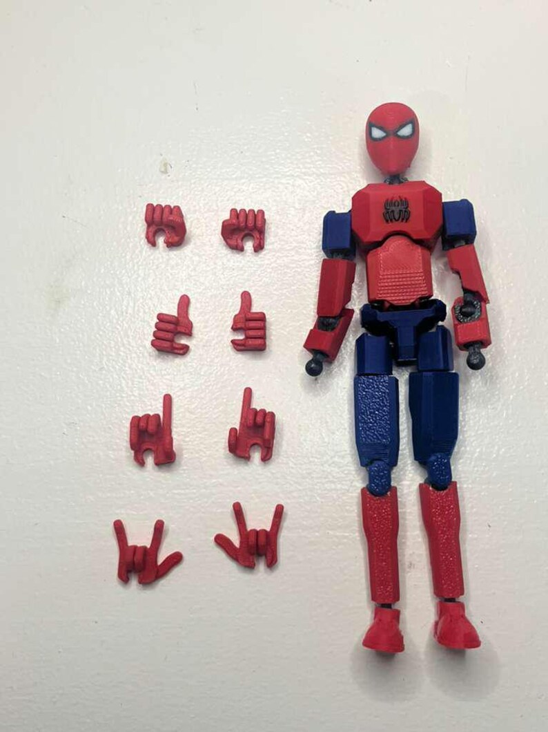 May include: A red and blue articulated action figure resembling Spider-Man, with interchangeable red hands in various gestures. The figure has a red head with white eyes, a red torso, blue arms and legs.