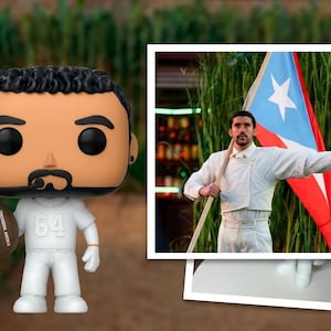 May include: A Funko Pop figure of a man in a white football uniform, holding a football. The figure has black hair and a mustache. In the background, a framed photo shows a man holding a Puerto Rican flag.