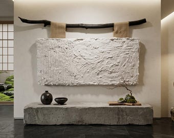 May include: A large rectangular white textured wall art piece hangs from a dark horizontal wooden branch by two beige fabric straps. Below, a long grey stone bench holds a dark ceramic vase, a small bowl, and a wooden tray with moss.