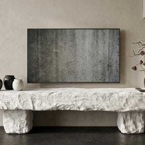 Puede incluir: Un banco largo y rectangular de piedra blanca con una superficie rugosa y texturizada, sostenido por dos patas de piedra en forma de bloque. Encima hay tres peque&ntilde;os jarrones de cer&aacute;mica en verde oliva, negro y blanco, una rama y un incensario.
