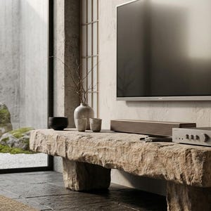 Puede incluir: Un televisor de pantalla plana montado en una pared texturizada sobre un banco de piedra largo y rectangular. El banco sostiene una barra de sonido horizontal, un amplificador electr&oacute;nico gris con perillas, un jarr&oacute;n de cer&aacute;mica y dos tazas.