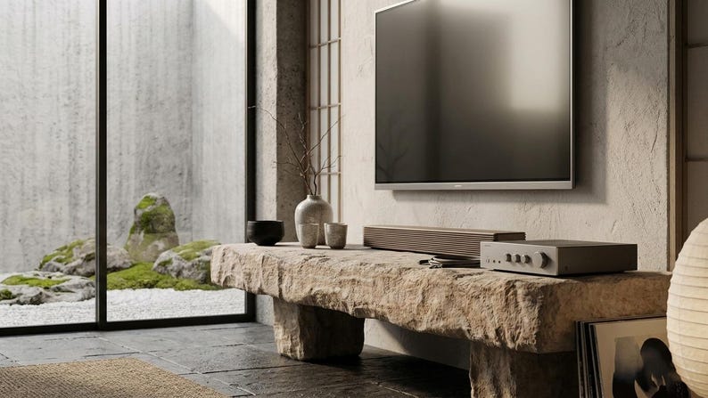 Puede incluir: Un televisor de pantalla plana montado en una pared texturizada sobre un banco de piedra largo y rectangular. El banco sostiene una barra de sonido horizontal, un amplificador electr&oacute;nico gris con perillas, un jarr&oacute;n de cer&aacute;mica y dos tazas.