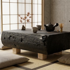 Peut inclure: Une table basse rectangulaire en bois noir avec une surface texturée, soutenue par quatre petits blocs de bois de couleur claire. La table est ornée d'une théière, de tasses et d'un vase avec des feuilles rouges. La scène se déroule sur un tatami avec des coussins.